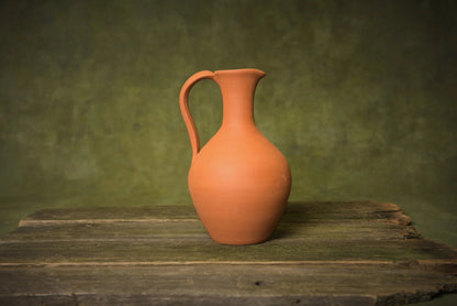 Handmade terracotta clay pitcher jug with handle on rustic wooden table, artisan homeware