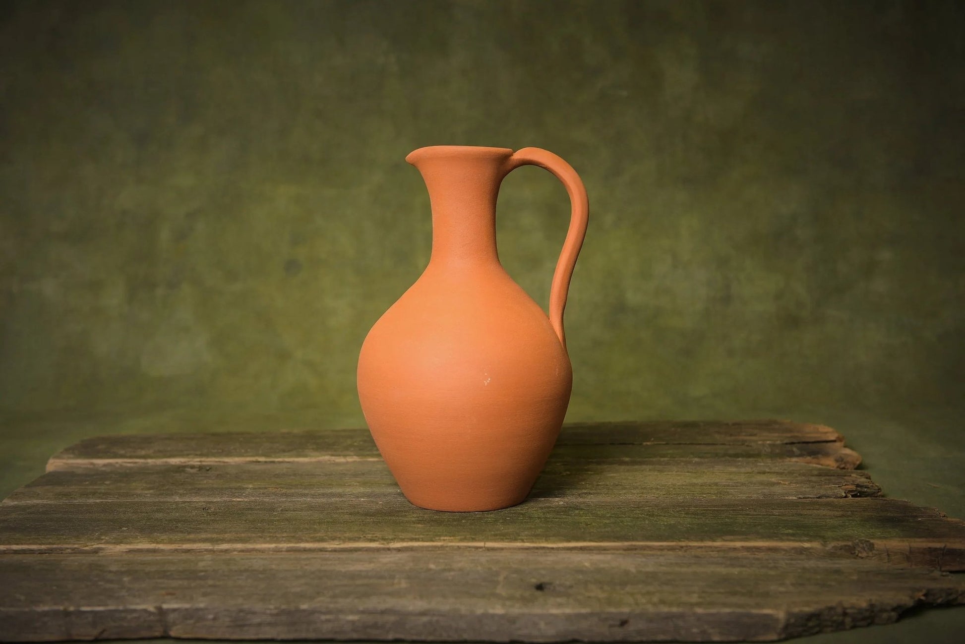 Handmade terracotta pitcher with handle on rustic wood, clay homeware decor product