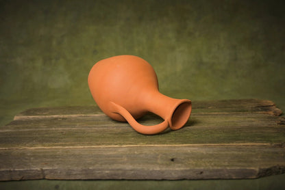 Handmade terracotta pitcher with handle on rustic wooden surface, unglazed ceramic homeware