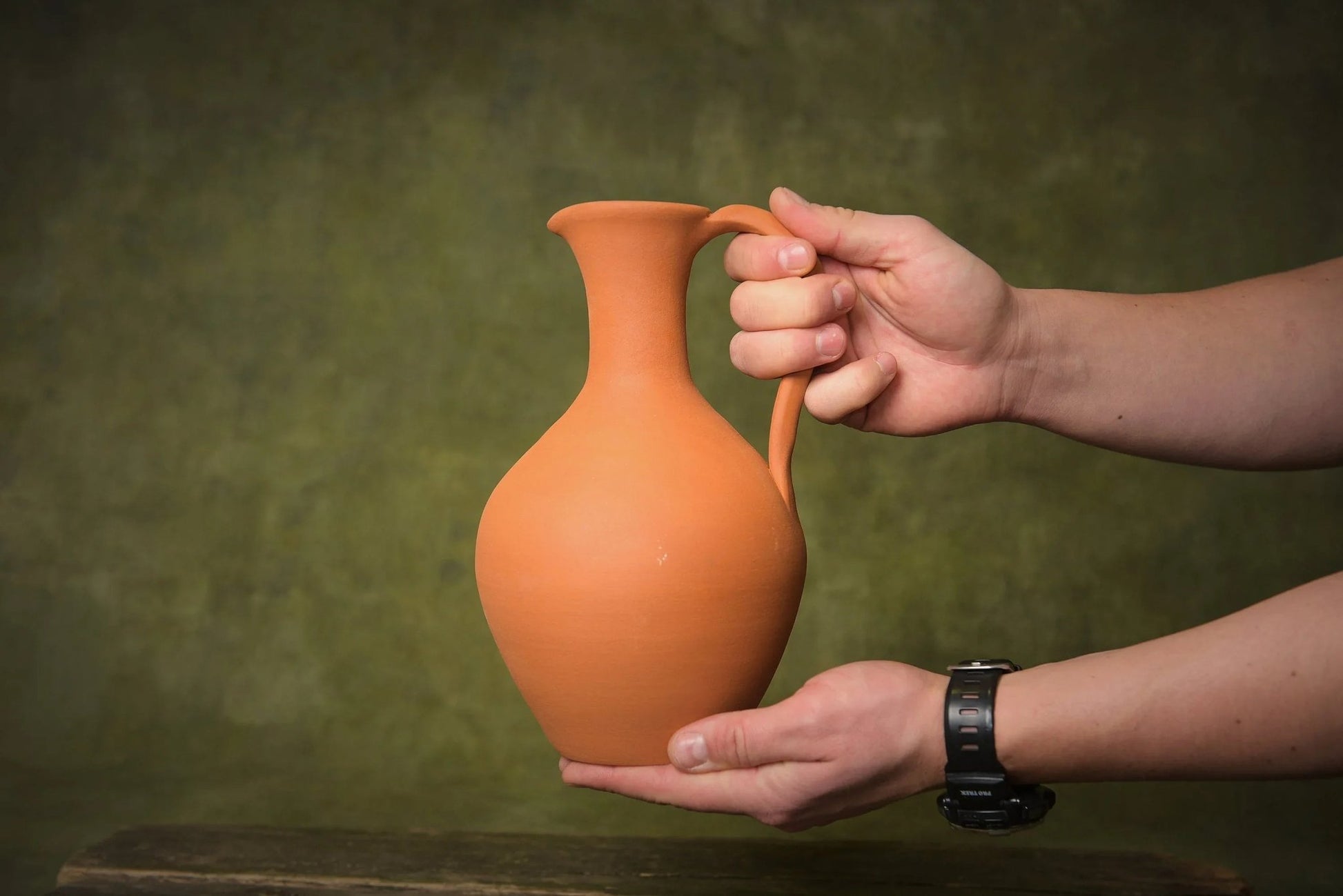 Handmade terracotta ceramic pitcher with handle, shown in hand, artisan clay homeware