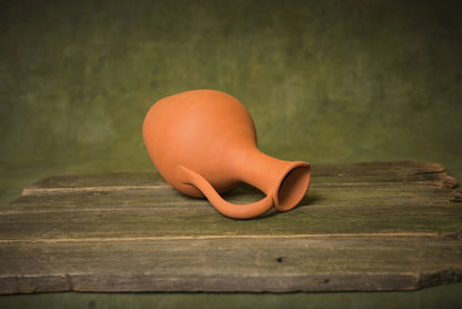 Handmade terracotta clay water jug with handle on rustic wood surface, artisan homeware