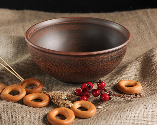 Handmade brown clay bowl on burlap cloth with bagels, wheat, and red berries, rustic homeware