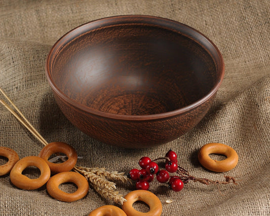 Handmade brown clay bowl with rustic finish, surrounded by bagels and red berries on burlap