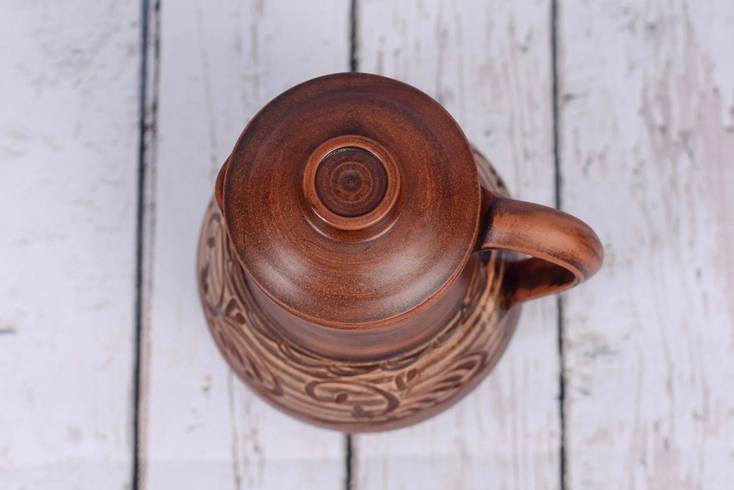 Handmade clay jug with lid and handle on rustic wood, artisan ceramic homeware
