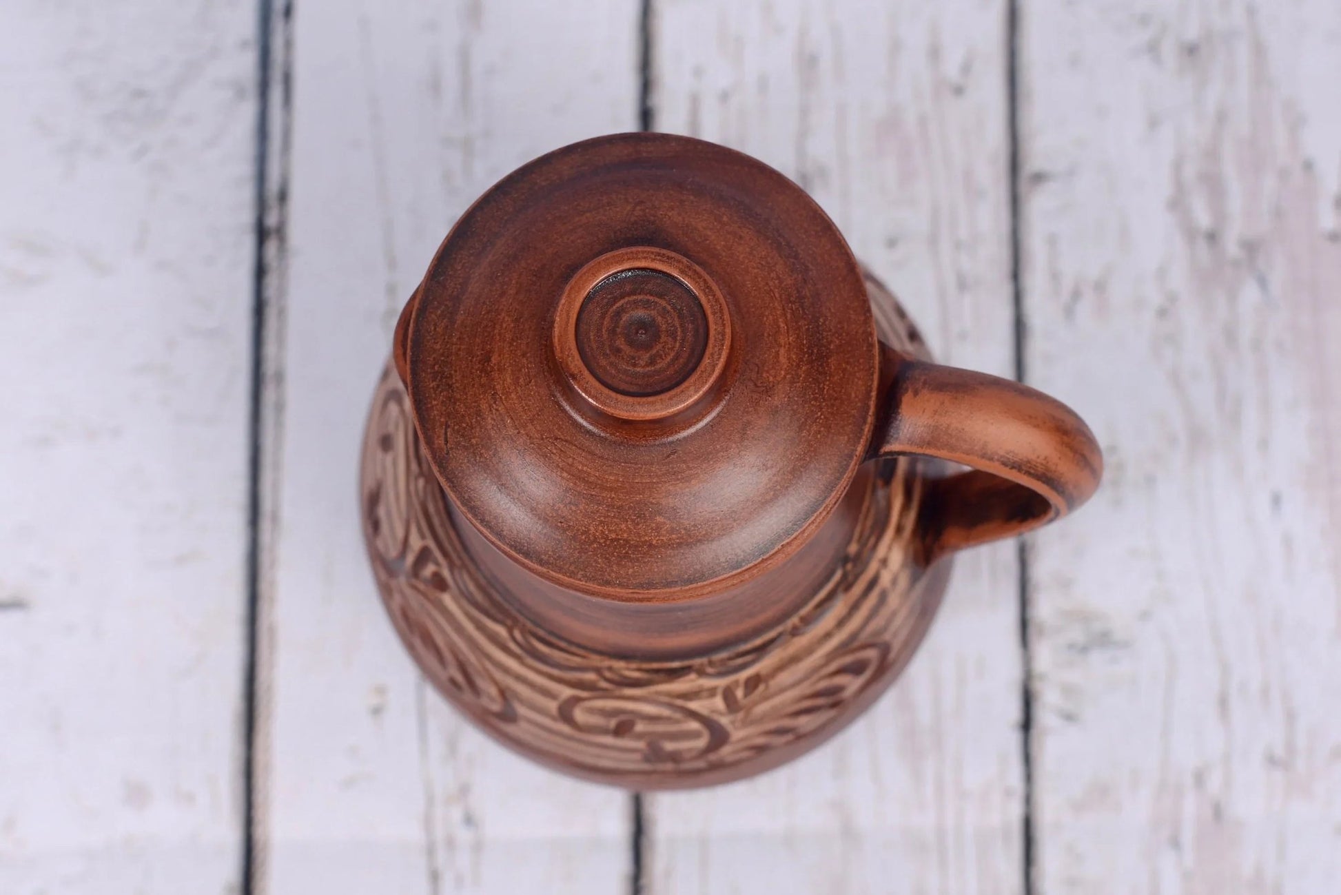 Handmade clay jug with lid and handle on rustic wood, artisan ceramic homeware