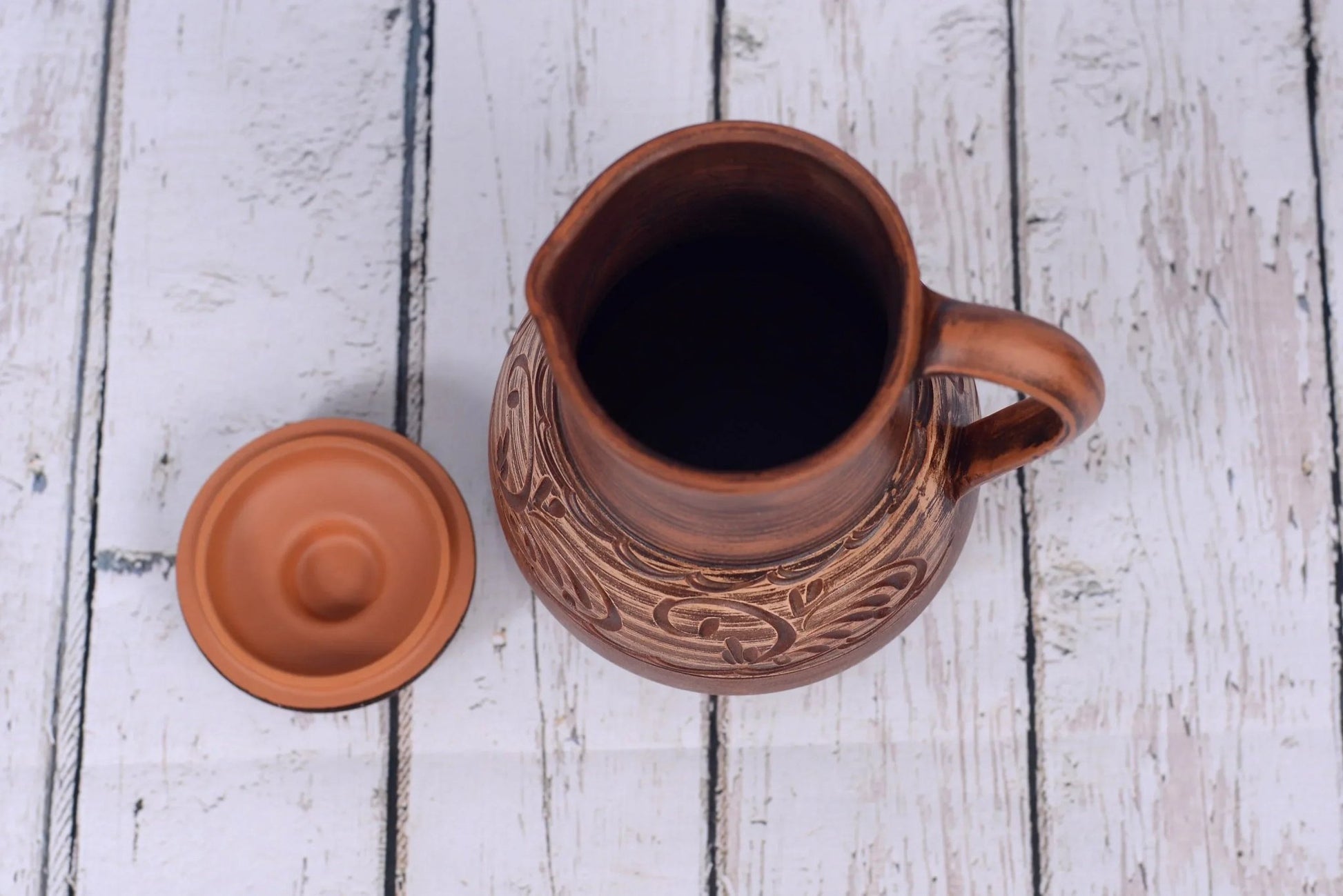 Handmade clay jug with lid, rustic ceramic pitcher on white wooden background