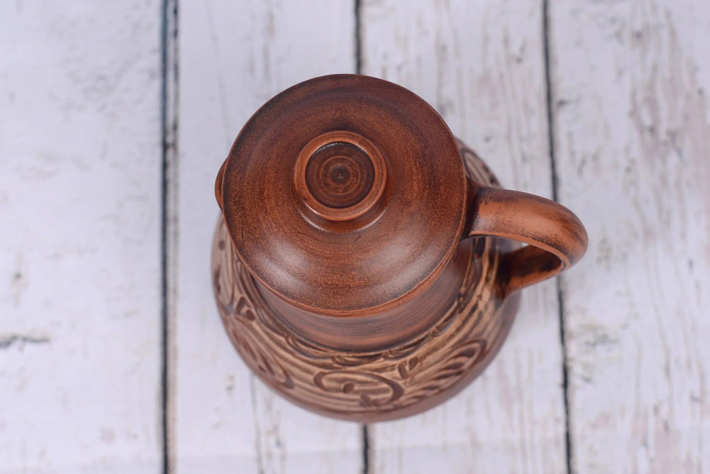 Handmade clay jug with lid and handle on rustic white wooden surface