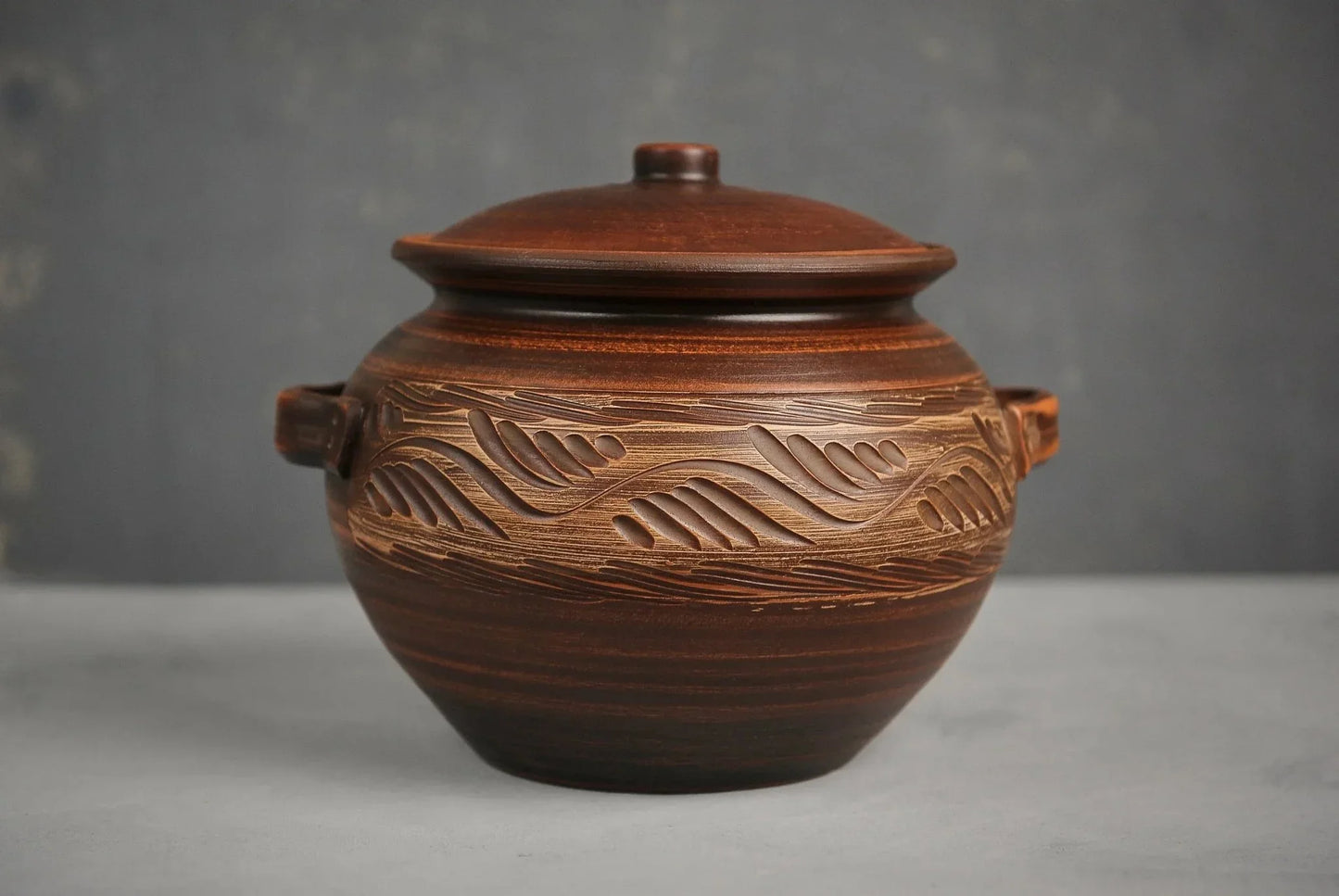 Handmade clay casserole dish with lid and carved pattern, artisan ceramic cookware on gray backdrop