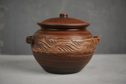 Handmade clay casserole dish with lid and carved pattern, artisan ceramic cookware on gray backdrop
