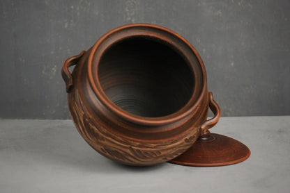 Handmade clay casserole pot with lid and handles, artisan ceramic bakeware on gray background