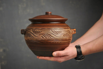 Hand holding a large handmade clay ceramic baking dish with carved pattern, rustic cookware