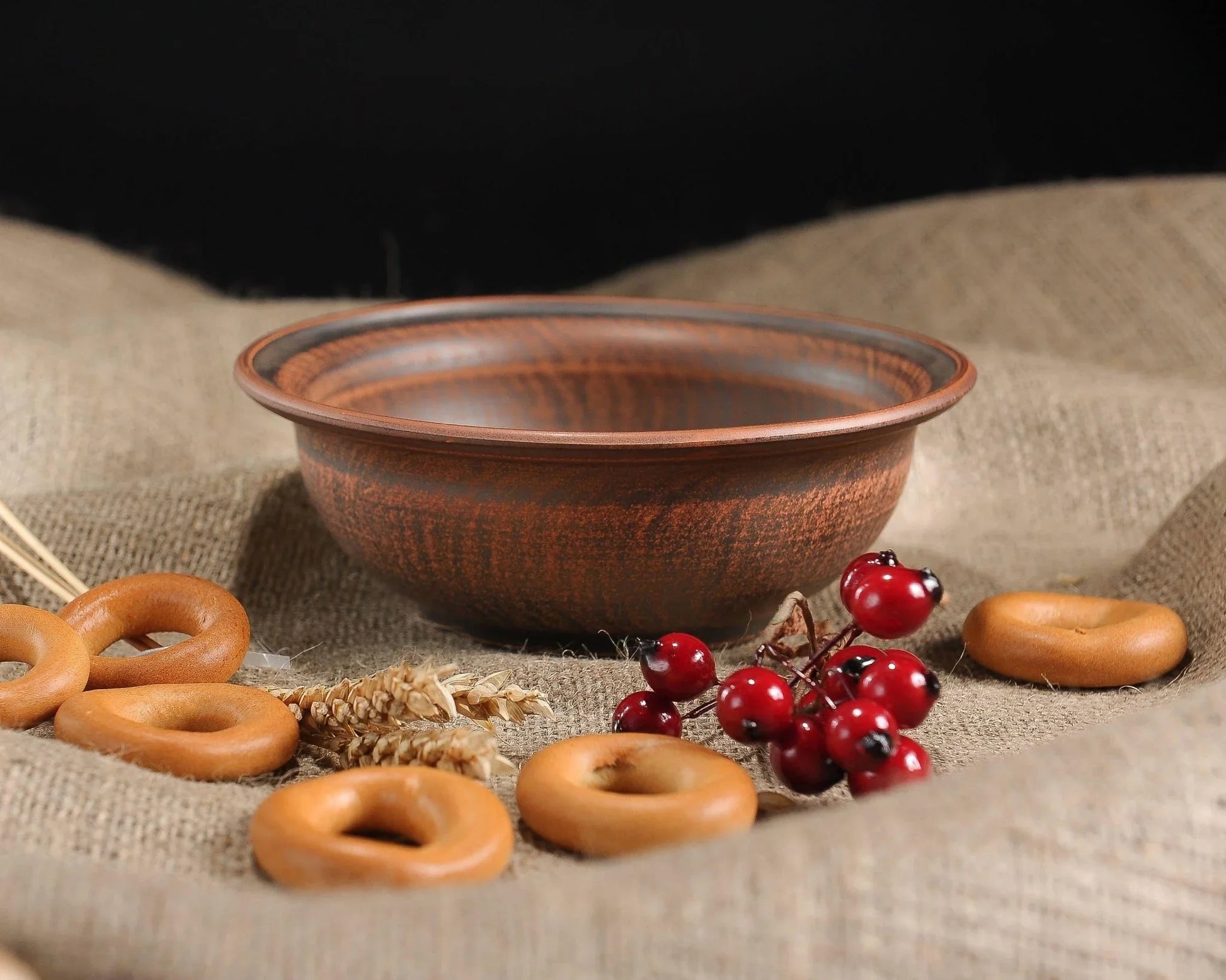 Handmade brown clay bowl with bagels and red berries on burlap, artisan pottery homeware