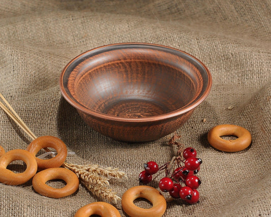 Handmade brown clay bowl on burlap with red berries and bakery rings, artisan pottery homeware