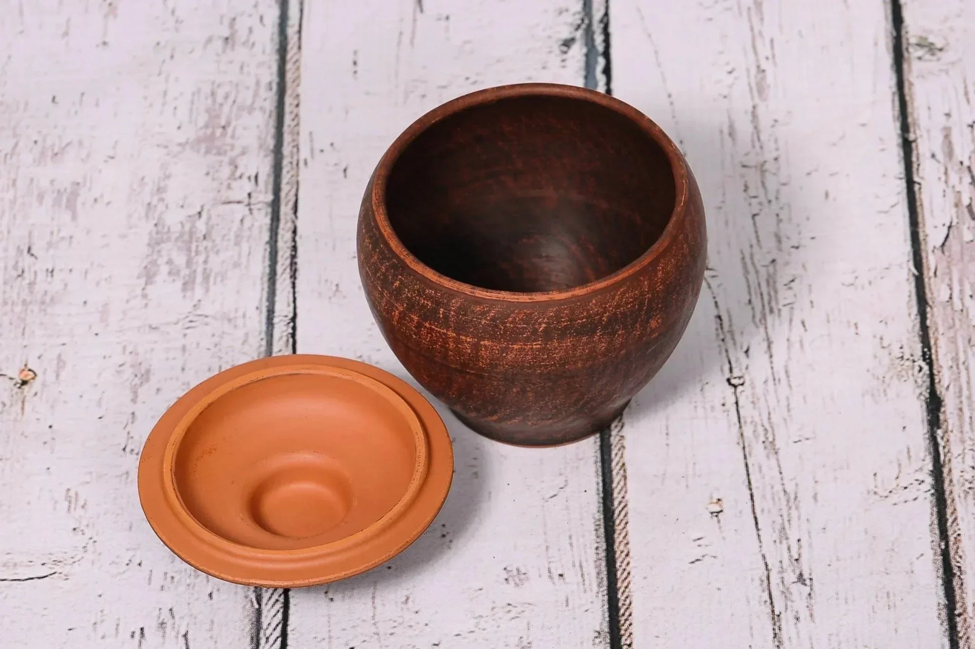 Handcrafted ceramic clay baking pot with lid on rustic wood surface, artisan homeware