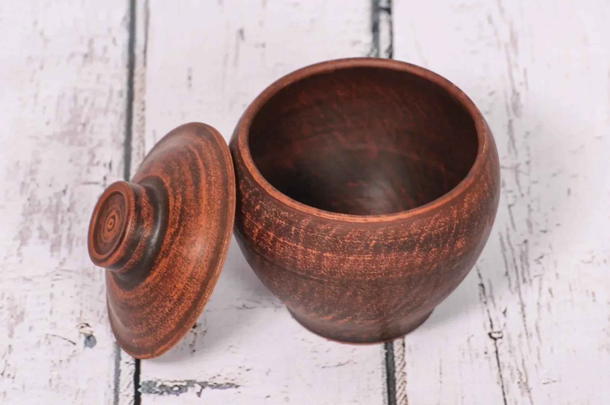 Handmade clay pot with lid, rustic ceramic cookware from clayproductsshop, on white wood.