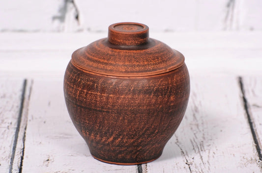 Handcrafted ceramic clay pot with lid on rustic white wooden background