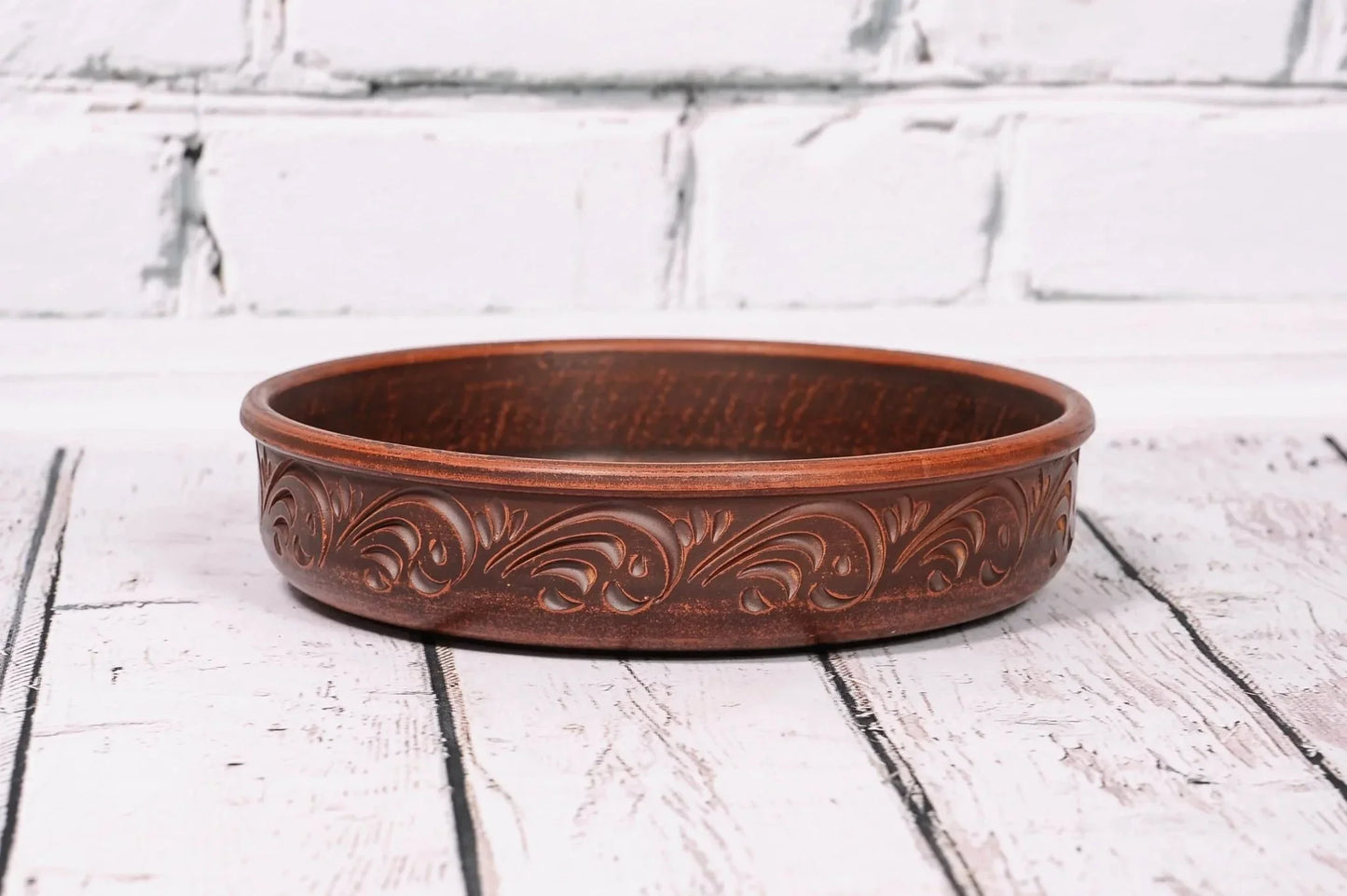 Handcrafted round ceramic baking dish with ornate clay pattern, displayed on wood surface