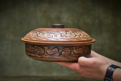 Hand holding handmade ceramic baking pot with decorative clay design, artisan cookware