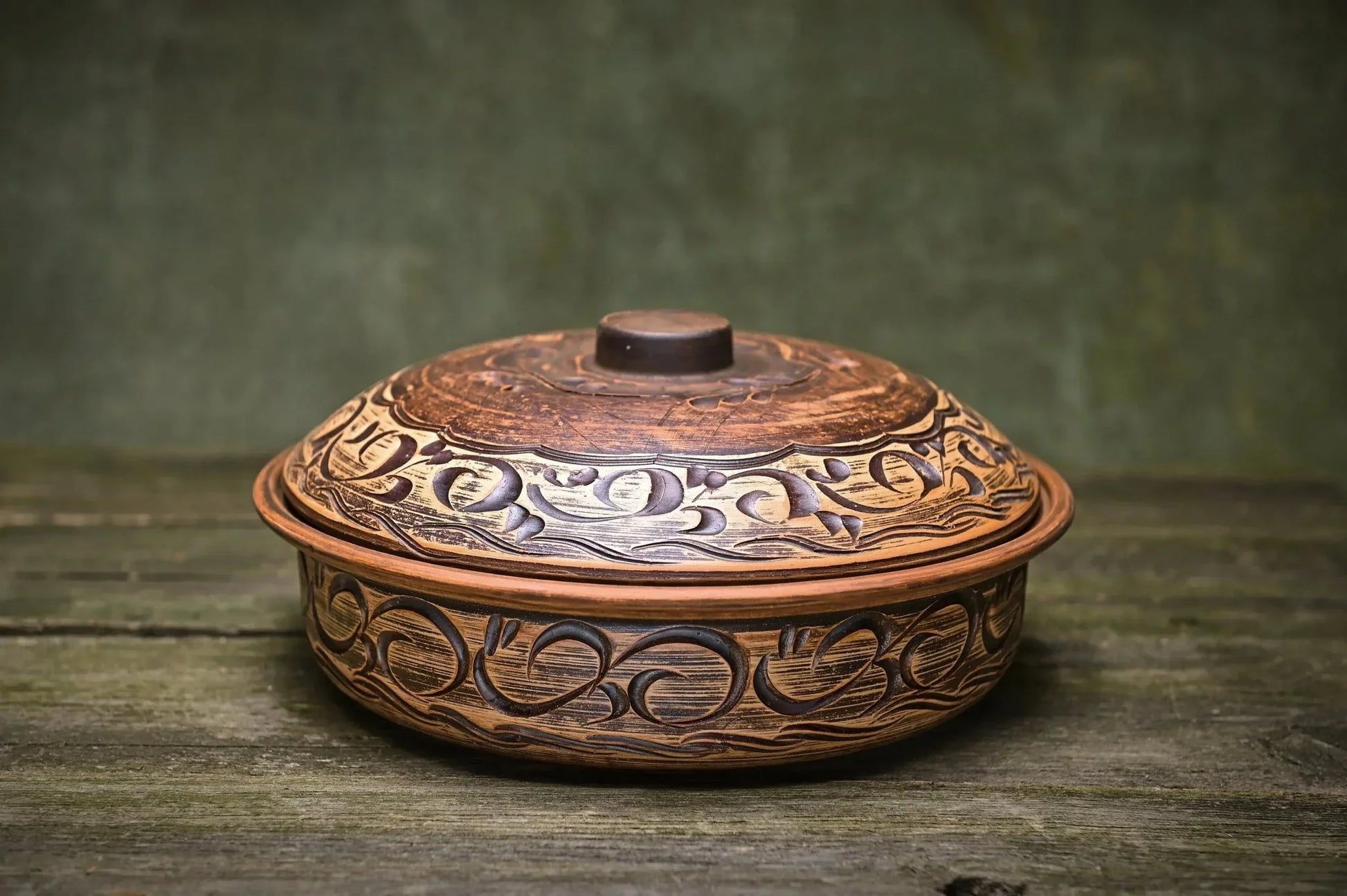 Handmade ceramic baking pot with artistic carvings, clay cookware on rustic wooden surface