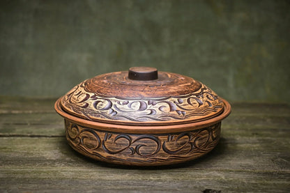 Handmade ceramic baking pot with artistic carvings, clay cookware on rustic wooden surface