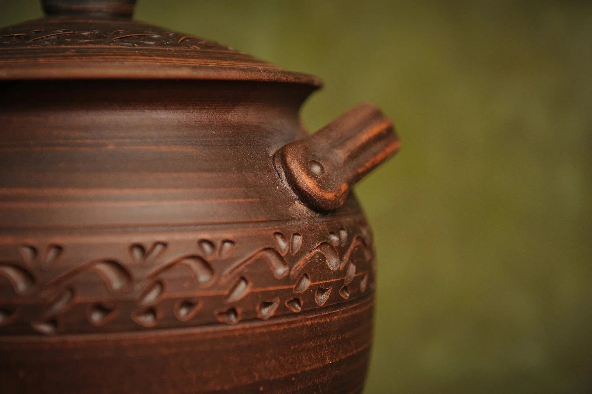 Handmade clay casserole pot with lid, decorative handle, and carved floral pattern