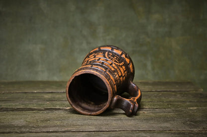 Handcrafted ceramic beer mug in red clay with carved patterns on rustic wood table