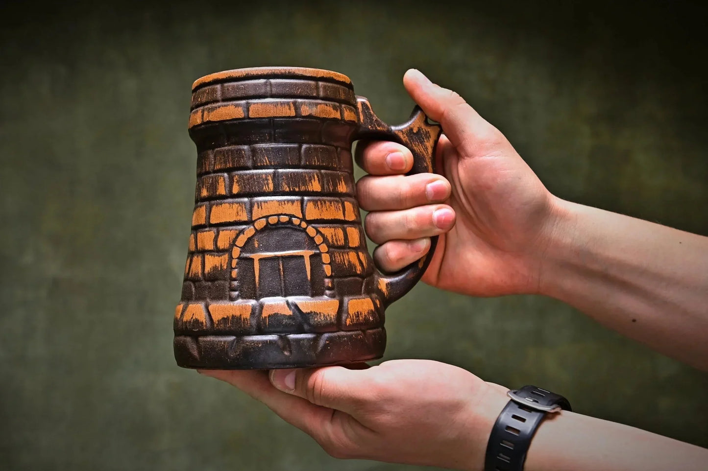 Hand holding a handcrafted red clay beer mug with rustic brick pattern, artisan pottery product