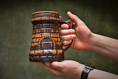 Hand holding a handcrafted red clay beer mug with rustic brick pattern, artisan pottery product