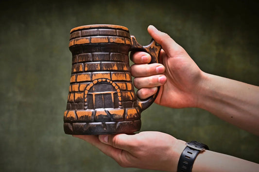 Hand holding a handcrafted red clay beer mug with rustic brick pattern, artisan pottery product