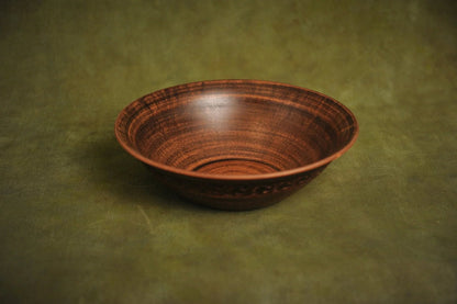 Handmade red clay ceramic bowl with textured finish on green background