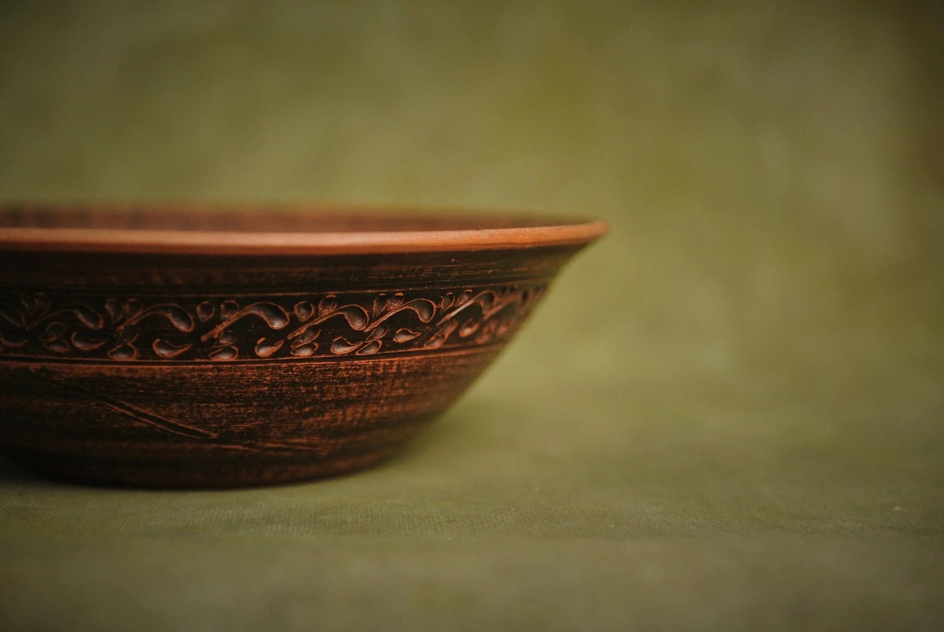 Handmade brown ceramic bowl with ornate clay detailing on a green background