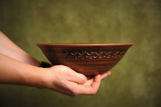 Hand holding artisan handmade brown clay ceramic bowl with decorative pattern