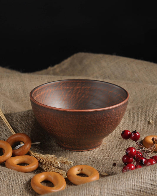 Handmade brown ceramic clay bowl on burlap with bagels and red berries, artisan homeware