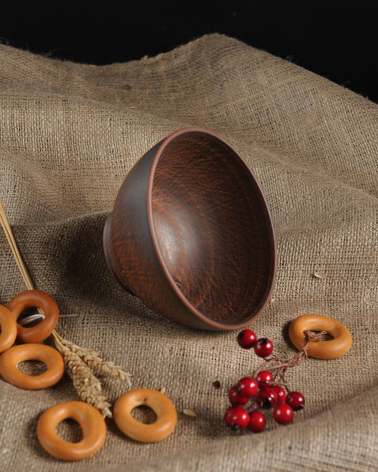 Handmade brown ceramic clay bowl on burlap with bread rings and red berries, artisan pottery