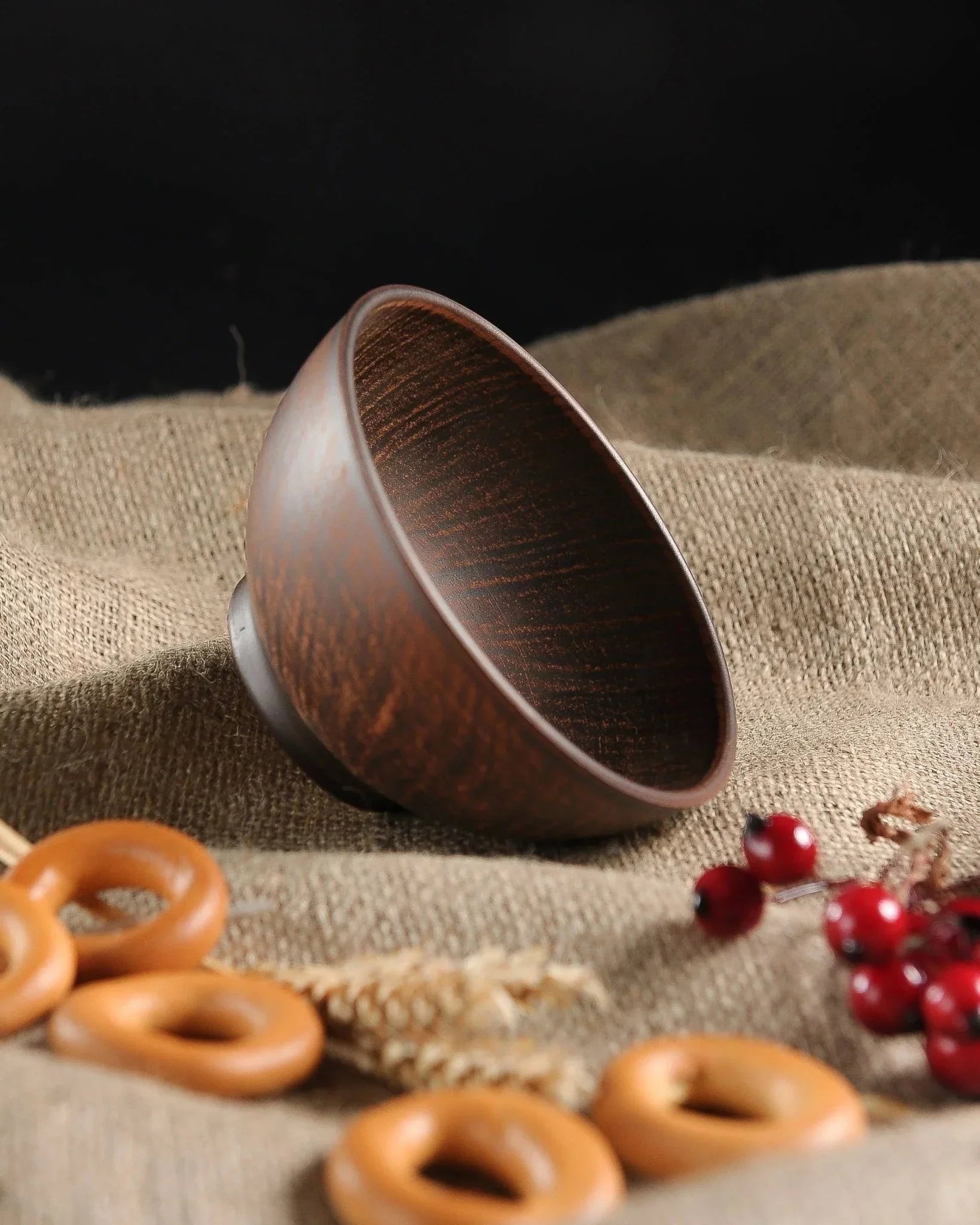 Handmade brown ceramic clay bowl on burlap with bagels, wheat, and red berries