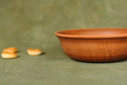 Handmade brown ceramic clay bowl on green fabric, artisan homeware product