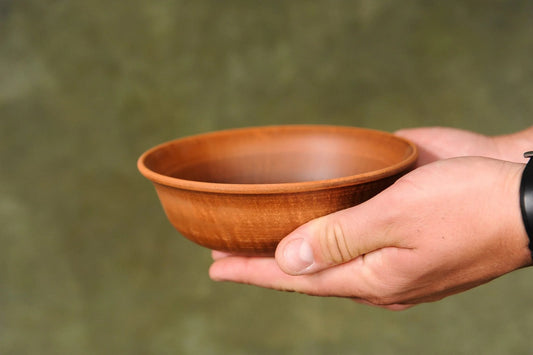 Hand holding a handmade brown clay ceramic bowl with matte finish, rustic homeware