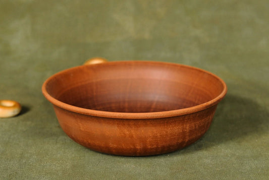 Handmade unglazed ceramic clay bowl with brown pottery finish on a green cloth surface