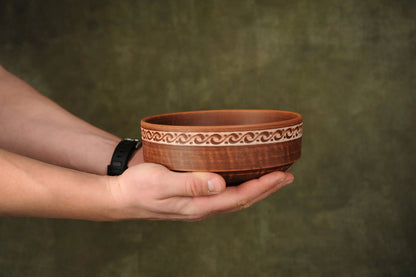 Hand holding a handmade rustic earthenware clay bowl with carved pattern, eco pottery
