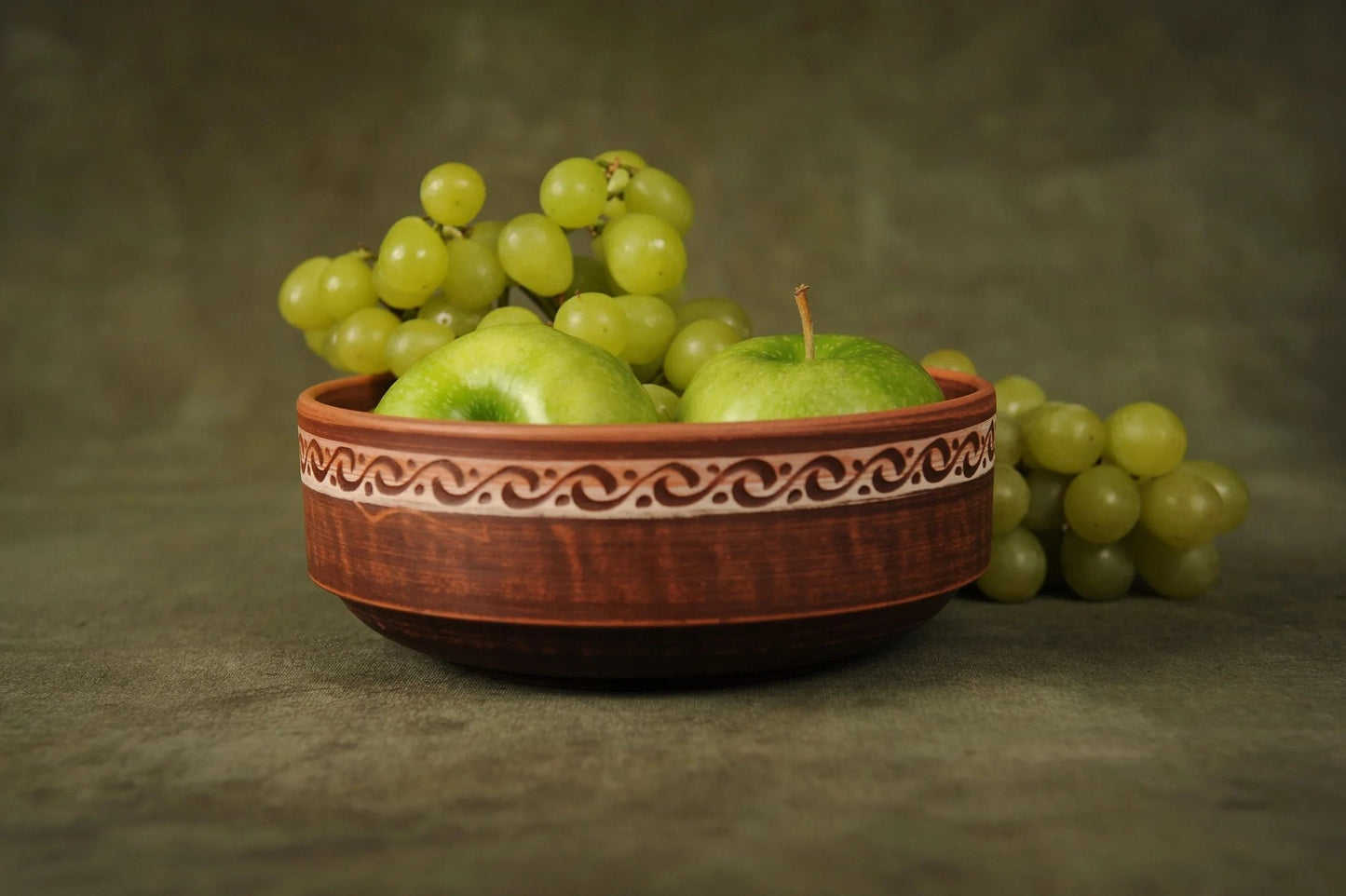 Handmade rustic clay bowl with green apples and grapes, artisan earthenware home decor