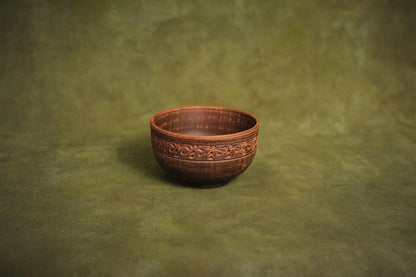 Handmade deep red clay ceramic bowl with ornate rim on a green background, Ukrainian pottery