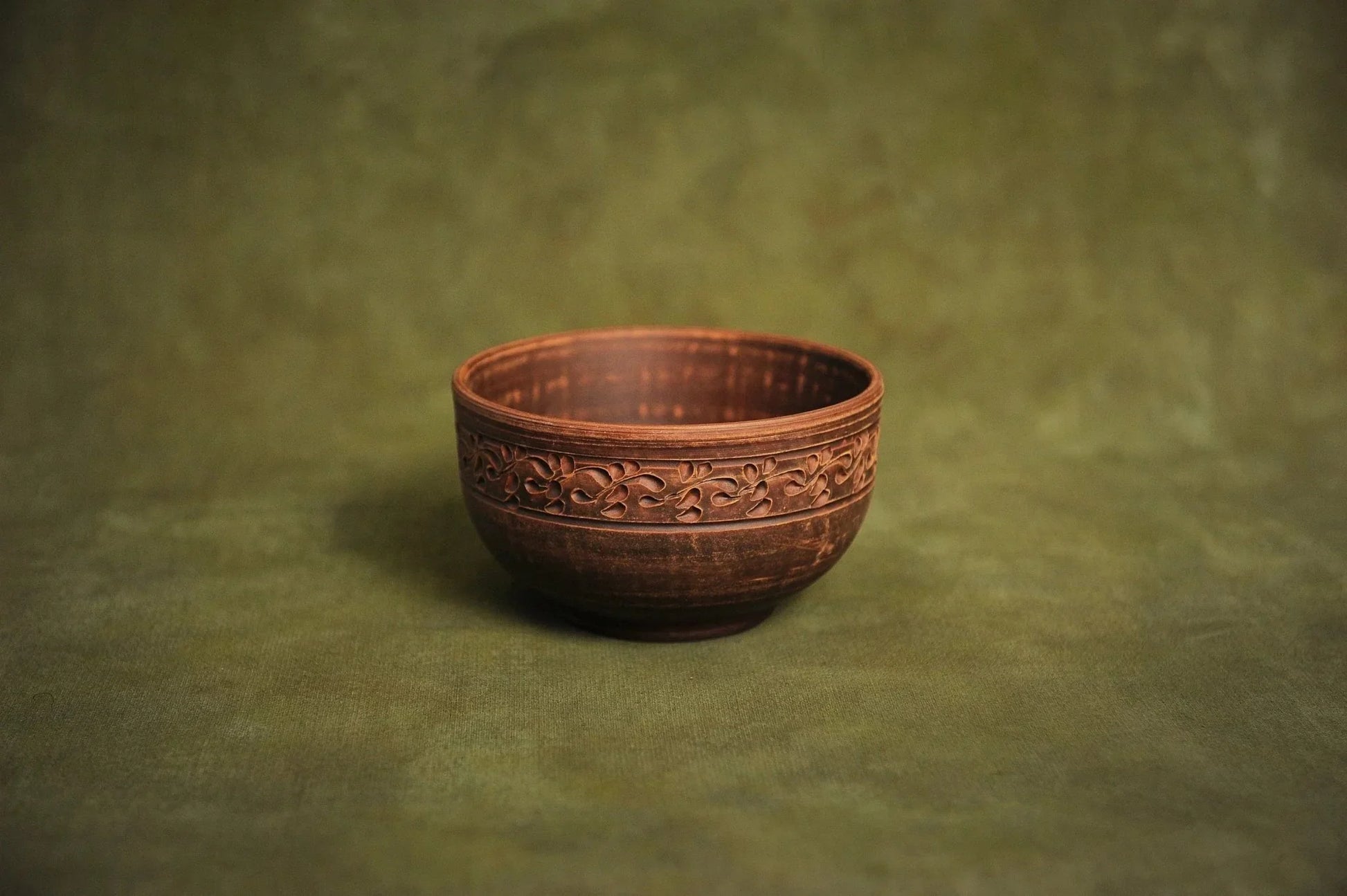 Handmade deep red clay bowl with ornate rim, Ukrainian pottery on green background