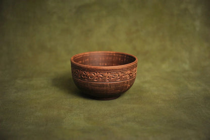Handmade deep red clay bowl with ornate rim, Ukrainian pottery on green background