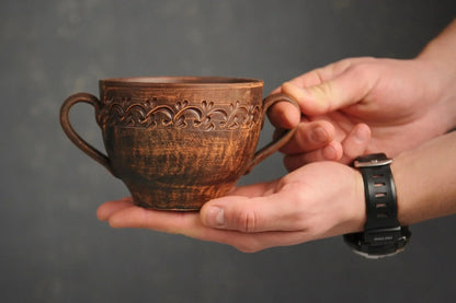 Handmade clay soup bowl with handles and ornate carved pattern, held in hands, artisan pottery