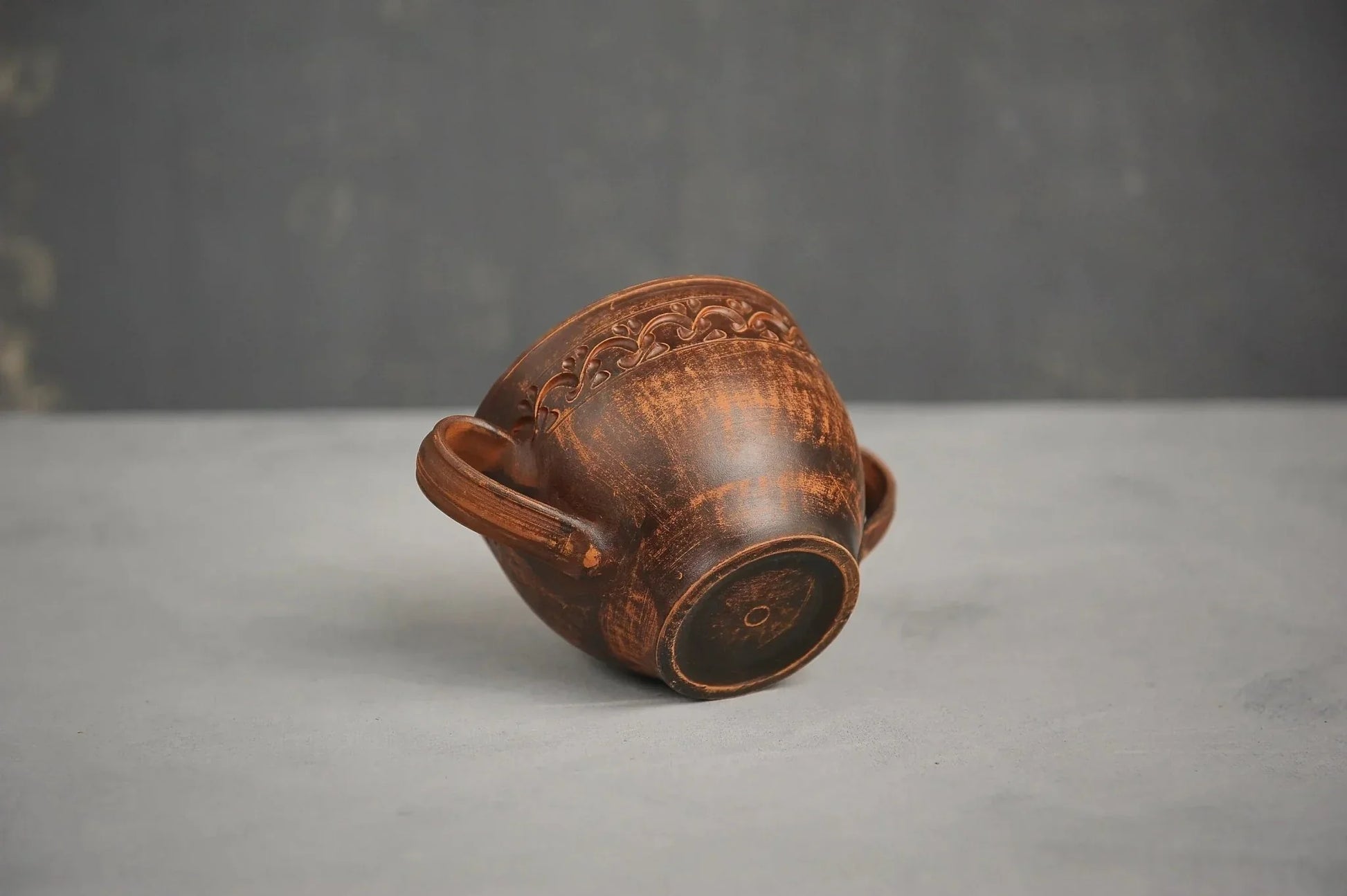 Handmade brown ceramic bowl with two handles, artisan Ukrainian pottery on a gray background