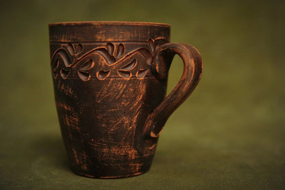 Handmade red clay ceramic cup with hand-engraved ethnic pattern on rustic green background