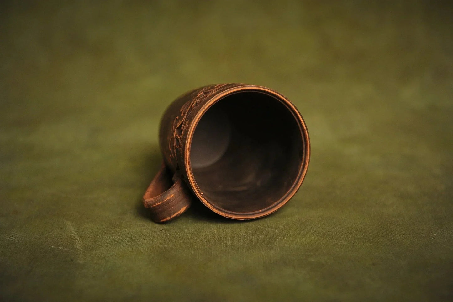 Handmade red clay ceramic cup with engraved ethnic design on green background