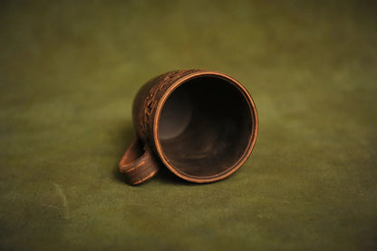 Handmade red clay ceramic cup with engraved ethnic design on green background