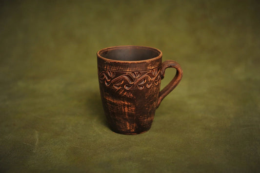 Handmade red clay ceramic cup with engraved ethnic design on green background