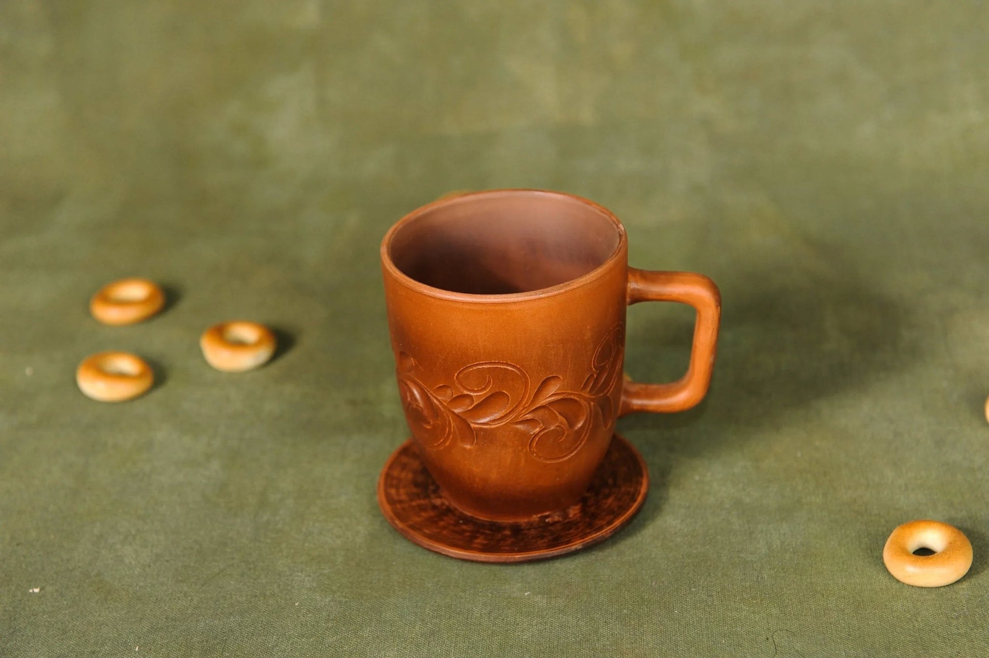 Handmade clay ceramic cup with saucer, artisan pottery mug on green background